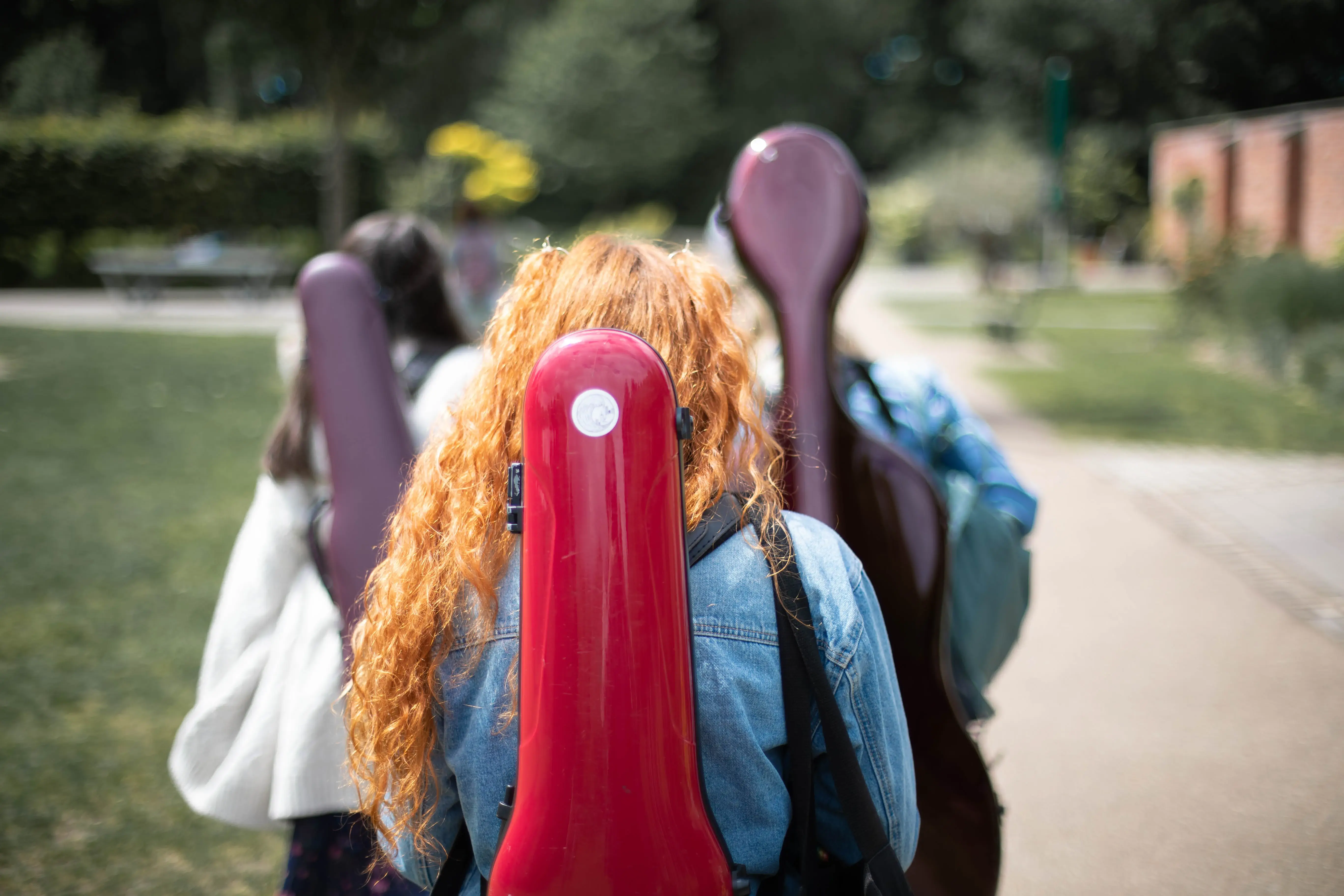 image from behind violinist with case on her back walking. cello and violin also in background.